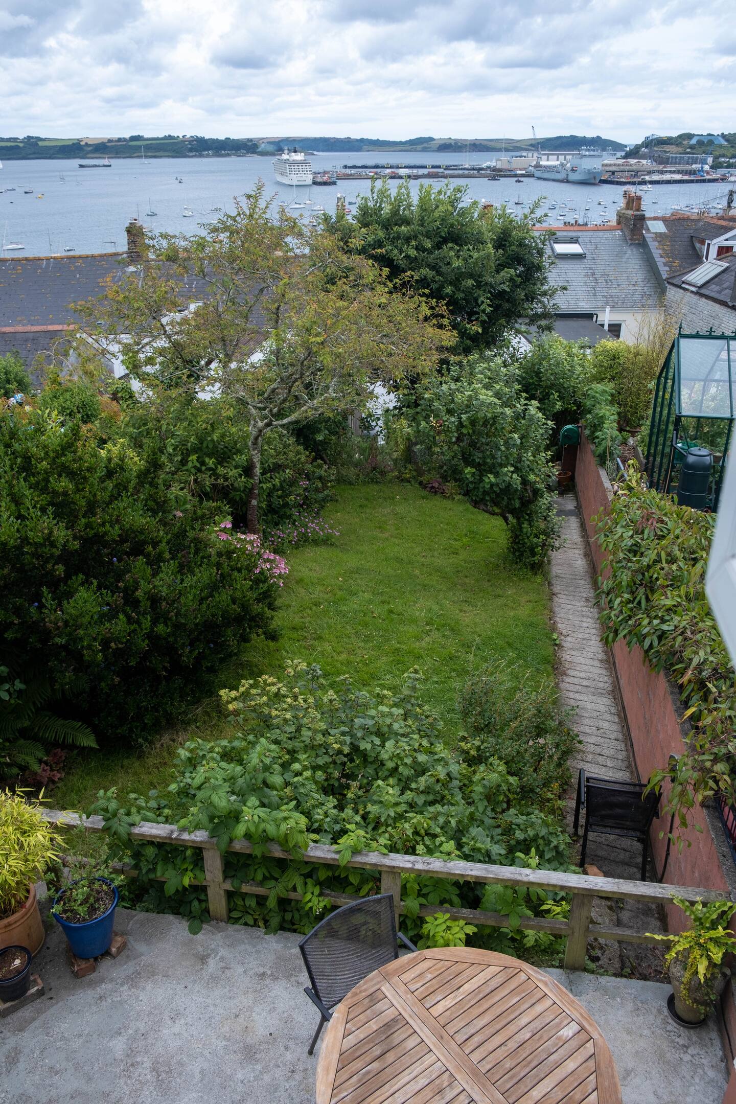 Patio table overlooking a long green garden with Falmouth harbour beyond